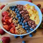 A delicious and visually appealing granola parfait layered with creamy Greek yogurt, fresh strawberries, blueberries, and diced peaches, topped with crunchy granola