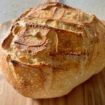 Golden homemade sourdough bread with a crispy crust and soft, airy interior, freshly sliced on a wooden cutting board