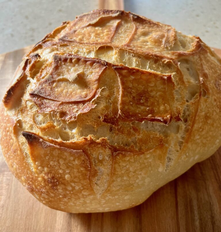 Golden homemade sourdough bread with a crispy crust and soft, airy interior, freshly sliced on a wooden cutting board